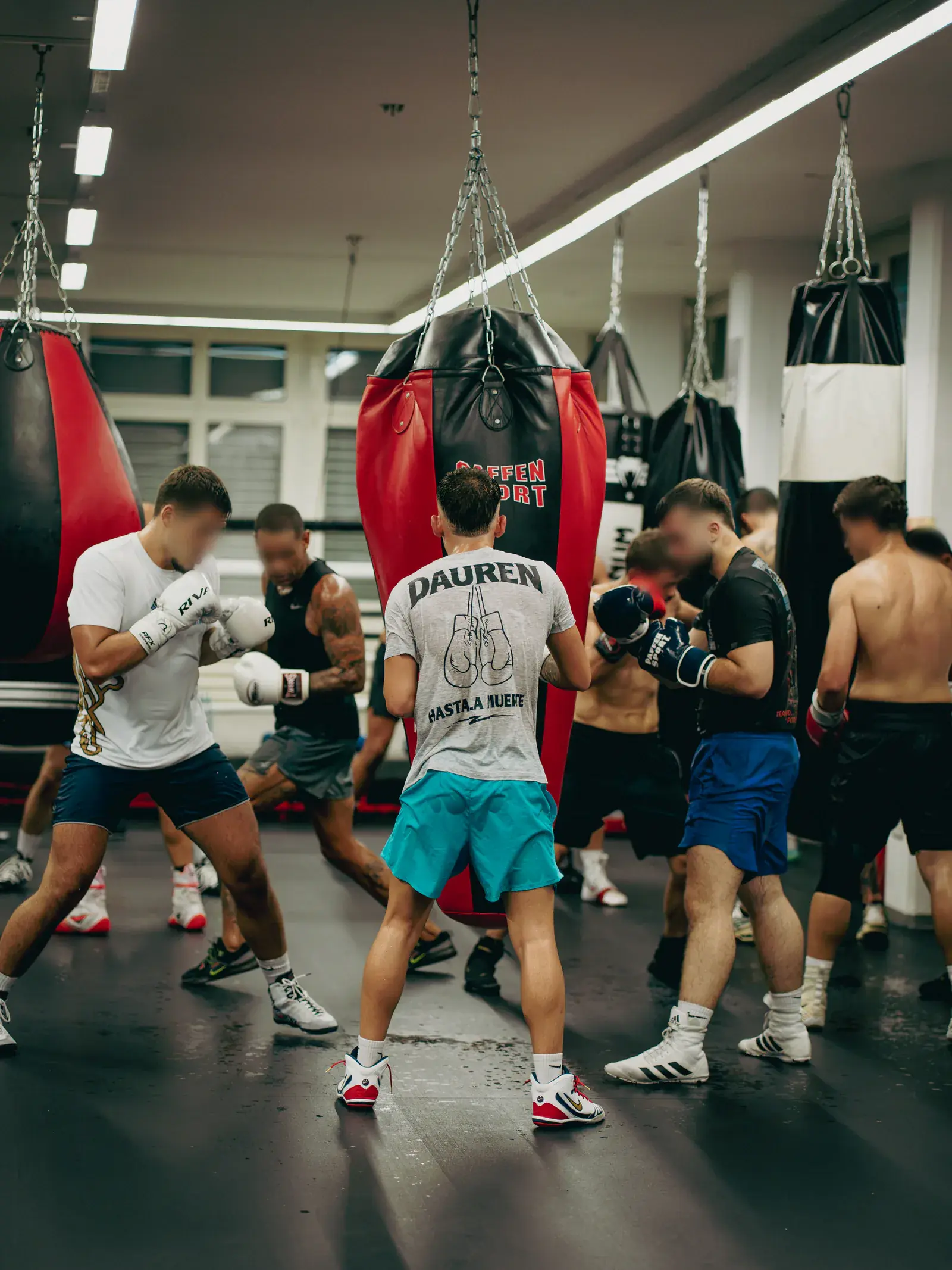 Mehrere Boxer mit Handschuhen üben paarweise zwischen roten und schwarzen Sandsäcken.