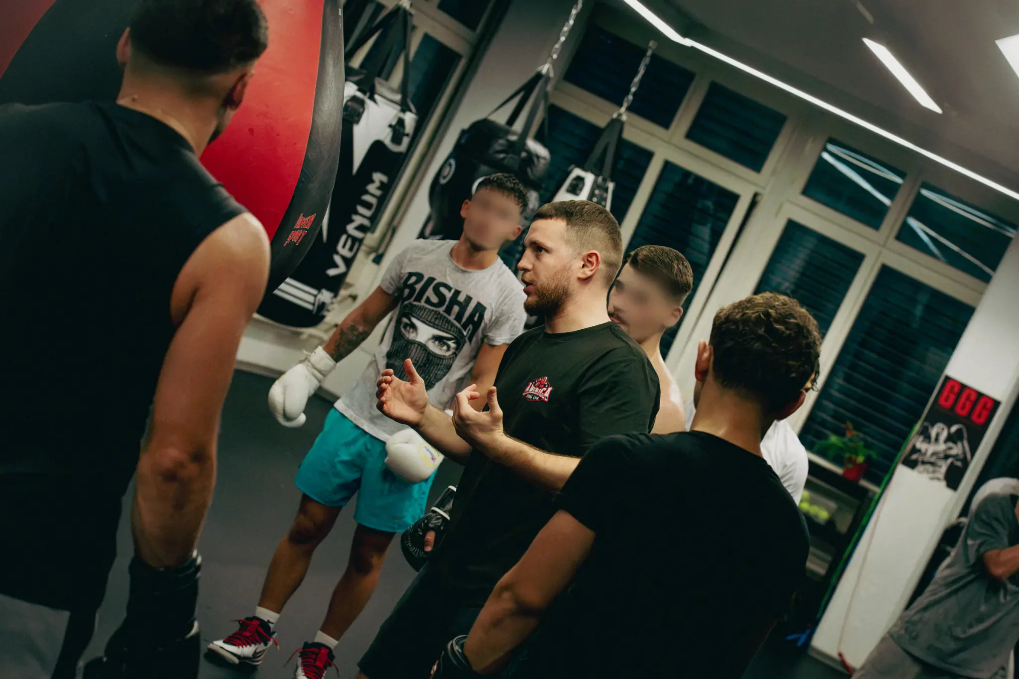 Coach im schwarzen America-Boxing-Shirt erklärt einer Gruppe von Boxern mit Handschuhen die nächste Übung.