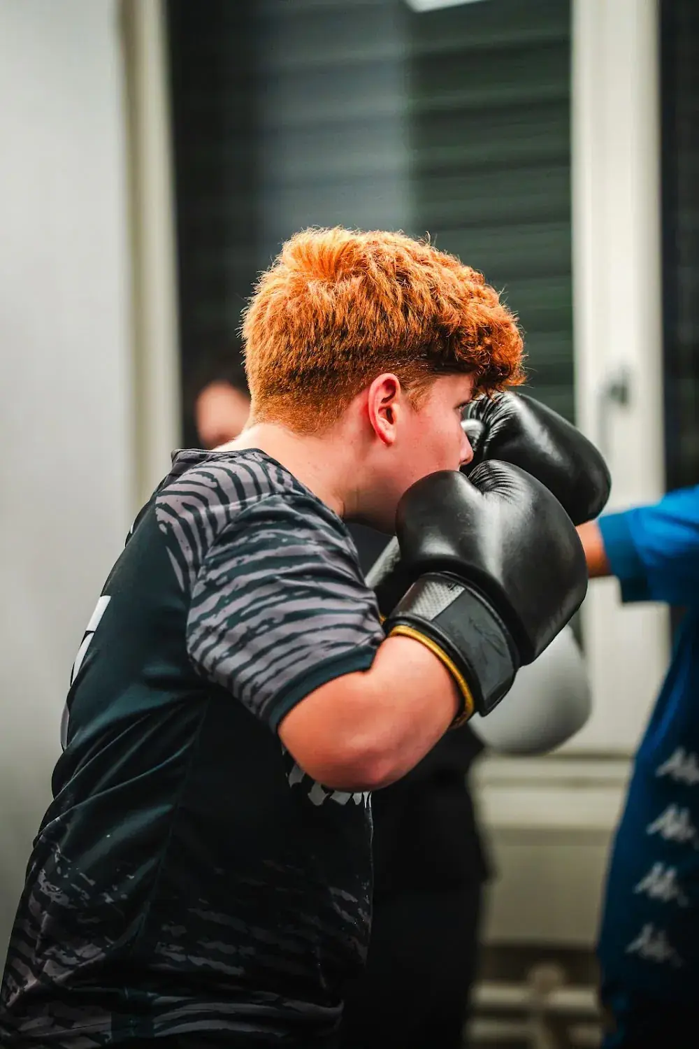 Junge mit schwarzen Boxhandschuhen hält im Kids-Training die Deckung vor dem Gesicht.