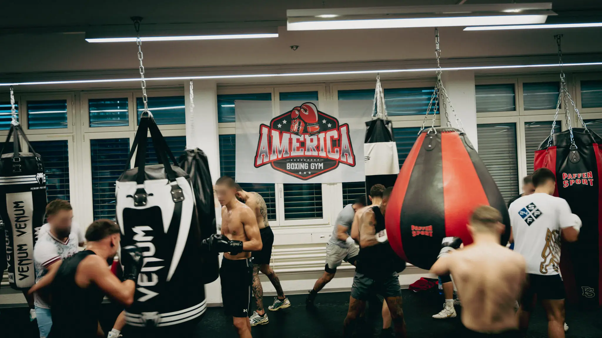 Trainingsgruppe an den Sandsäcken im America Boxing Gym, dahinter das Banner mit dem Gym-Logo.